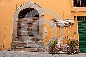 Red bike full of flowers standing in front of an old wooden door