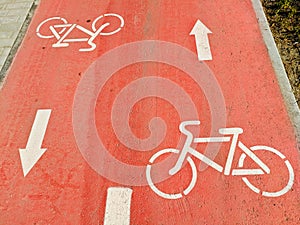 On the red bike path are white signs for the movement of bicycles in different directions