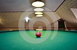 Red billiard ball on a green billiard table under lamps