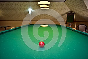 Red billiard ball on a green billiard table under lamps