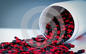 Red-black antibiotic capsule pills spill out of white plastic bottle container. Pharmaceutical industry. Prescription drug.