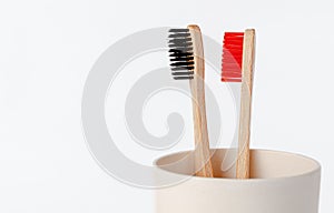 Red and black bamboo toothbrushes in eco cup on white background. Copy space
