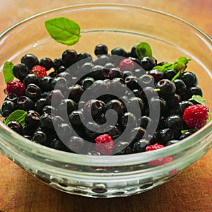 Red and black berries in a glass dish on a wooden background