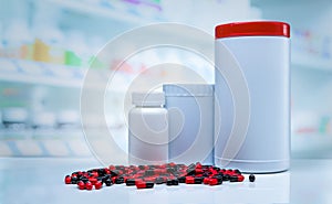 Red-black capsules pills spread on counter in drugstore. Blank label plastic drug bottle on blurred background of vitamins and