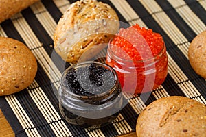 Red and black caviar in a jar with bread