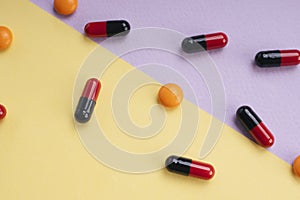 Red and black medicine pill capsule and orange circle pill over pastel background