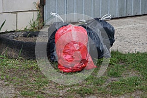 Red and black plastic bags of garbage in green grass outside