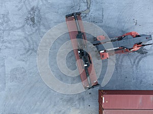 A red and black reach stacker lifting a brown shipping container in an inland port.