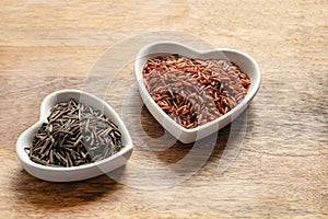 Red and black rice long grains in a heart shaped plate on wooden background