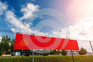 Red blank advertising banner hanging on a fence against the blue sky on a sunny day
