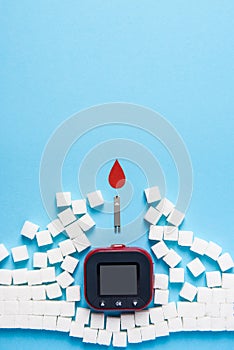 Red blood drop and wall made of sugar cubes ruined by Blood glucose test strips and Glucose meter on blue background