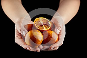 Person holging handful of half and whole red or blood oranges on black background