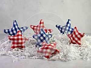 Red and Blue checkered fabric colored stars sitting on a bed of white paper shreds with a plaster background for the 4th of July