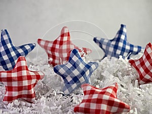 Red and blue checkered fabric covered stars sitting on a bed of white paper shreds with a plaster background for 4th of July,