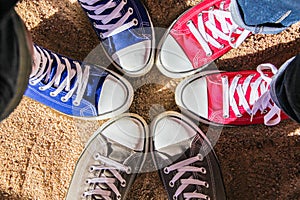 Red, blue and gray sneakers standing in the circle on dry sand, view from above . Friendship, fashion, lifestyle and adventure con