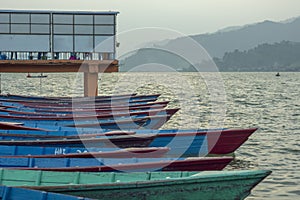 A red blue green wooden boats at the pier on the water in cloudy weather. lake on the background of the mountains