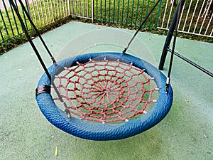 Red-blue hanging round swing made of braided rope with a wicker seat in a city playground