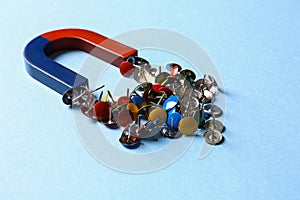 Red and blue horseshoe magnet attracting push pins on blue background