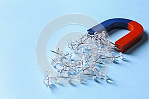 Red and blue horseshoe magnet attracting push pins on blue background