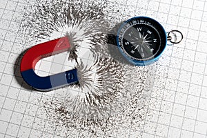 Red and blue horseshoe magnet or physics magnetic and compass with iron powder magnetic field on white paper graph background.