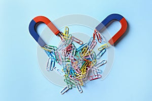 Red and blue horseshoe magnets attracting colorful paperclips on light blue background