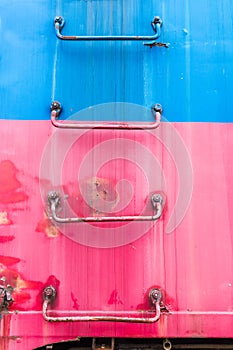 Red and blue metal rungs of a ladder going up the side of a train