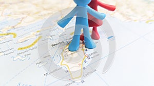 A red and blue rubber toy couple standing on the island of Rhodes on a map of Greece