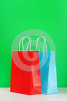 Red and blue shopping or gift bag on wooden desk against green background.