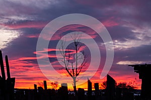 Red-blue sunset with dark clouds on the outskirts of the village. The outlines of an old broken fence against the backdrop of a