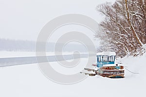 Red and blue tugboat stranded and covered with snow