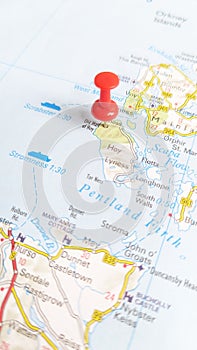 A red board pin stuck in the island of Hoy on a map of Scotland portrait