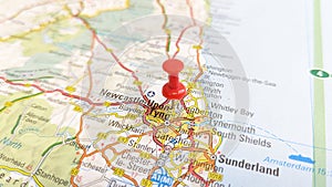 A red board pin stuck in Newcastle Upon Tyne on a map of England