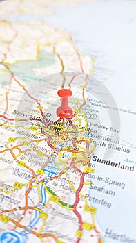 A red board pin stuck in Newcastle Upon Tyne on a map of England portrait