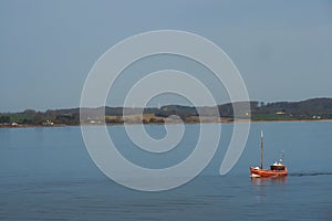 Red boat on the background of the shore with wind turbines, denmark coast, summer calm day, calm sea