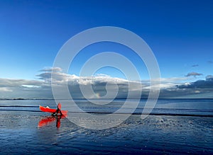 Red boat on the beach and rainbow over the calm sea.