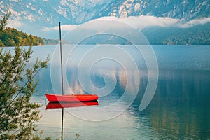 Red boat floating on tranquil lake Bohinj surface in summer morning photo