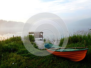 Red boat on the green shore against the background of the misty lake. Finland.