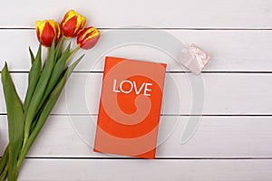 The red book Love lies on a white table. Flowers tulips and gift
