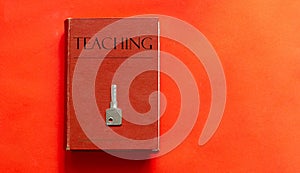 Red book with text TEACHING and a key on a red background