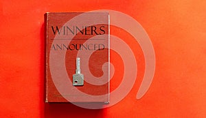 Red book with text Winners Announced and a key on a red background