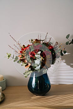 Red bouquet flower arrangement by florist with red roses, poppies and eucalyptus leaves in a blue vase on a wooden table