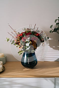 Red bouquet flower arrangement by florist with red roses, poppies and eucalyptus leaves in a blue vase on a wooden table