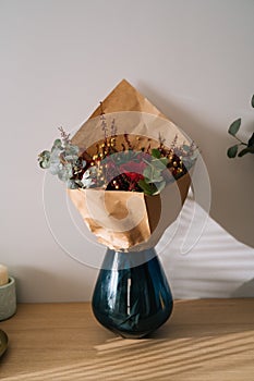 Red bouquet flower arrangement by florist with red roses, poppies and eucalyptus leaves in a blue vase on a wooden table