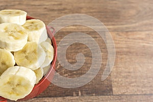 Red bowl with banana slices on wooden background