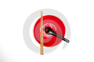 Red bowl with chopsticks and spoon on a white background. Top view