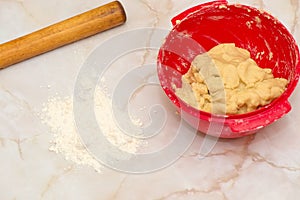 Red bowl with dough, rolling pin and flour powder on a table