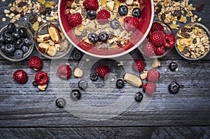 Red bowl with muesli, nuts and fresh berries on blue rustic background, top view, border