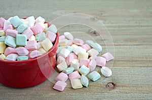 Red bowl overflowing with pastel butter mints on a wood background