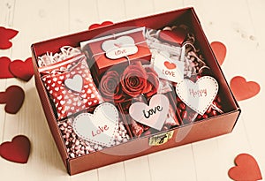 A red box filled with Valentine\'s Day gifts and candies, surrounded by more red and pink heart-shaped candies and small bags