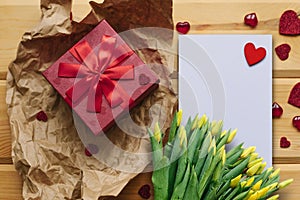 Red box with a gift and next to a white blank sheet for text with a heart on a wooden surface.